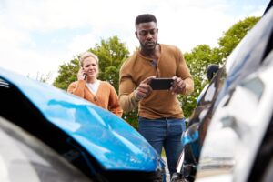man taking photos of car damage after an accident while woman is on the phone