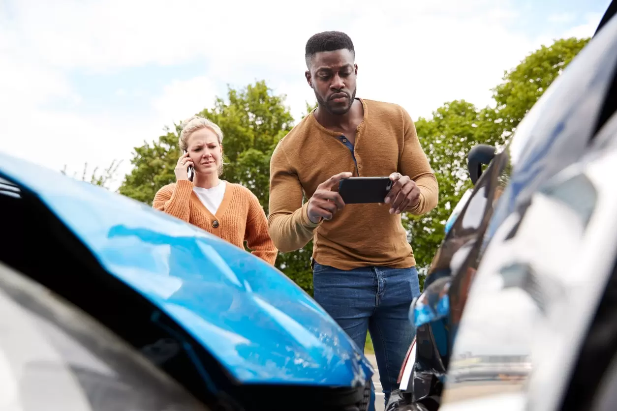 man taking photos of car damage after an accident while woman is on the phone