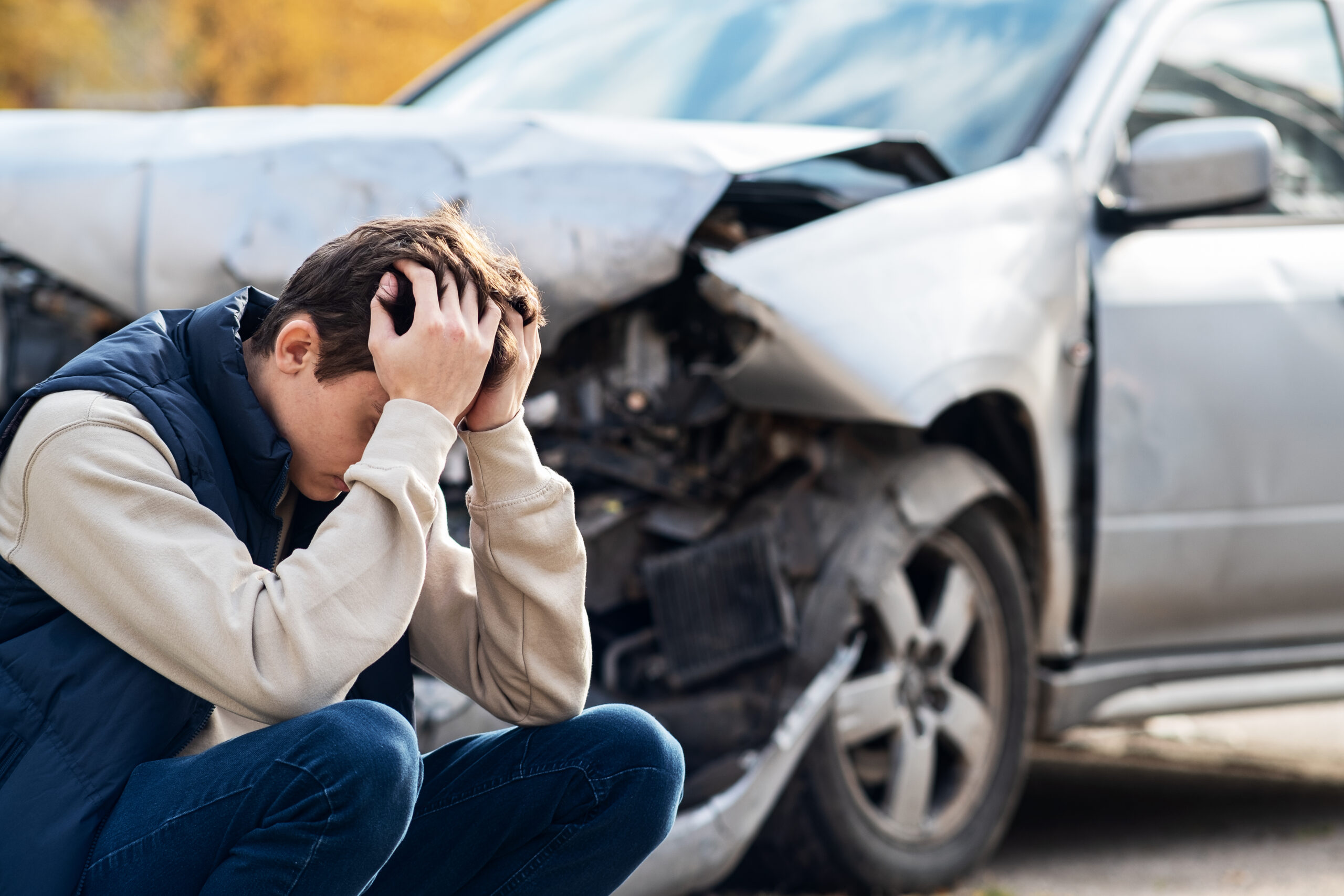 a man in distress crouching next to a damaged car after a car accident